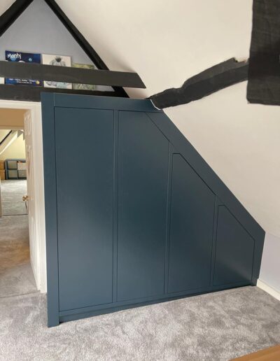 Bespoke modern handless wardrobe fitted to accommodate the sloping bedroom walls & floor, oak internals, push touch doors, finished in Farrow & Ball Hague blue.