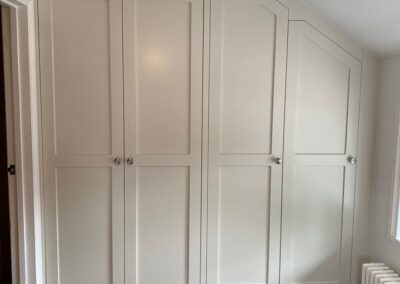 Bespoke shaker style wardrobe fitted into an alcove with a sloped ceiling with access to an adjacent room
