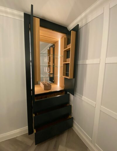 Custom-made handleless drinks cabinet with Lissa oak internals from Finsauk, push touch drawers, mirrored back & remote lights & feature wine storage drawer, finished in Neptune green paint