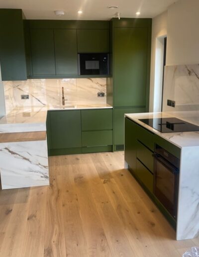 Bespoke contemporary kitchen designed & fitted with recessed handles, under-mounted lights on wall cupboards, oak breakfast bar, fitted integral appliances, finished in Farrow and Ball Bancha, client’s own Quartz worktops