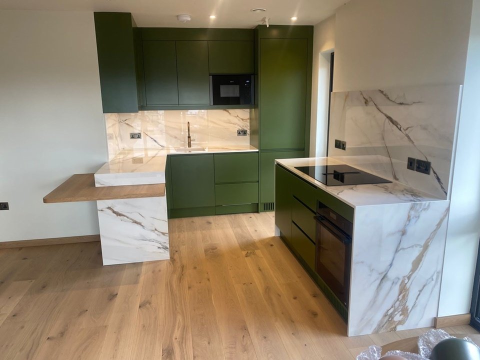 Bespoke contemporary kitchen designed & fitted with recessed handles, under-mounted lights on wall cupboards, oak breakfast bar, fitted integral appliances, finished in Farrow and Ball Bancha, client’s own Quartz worktops