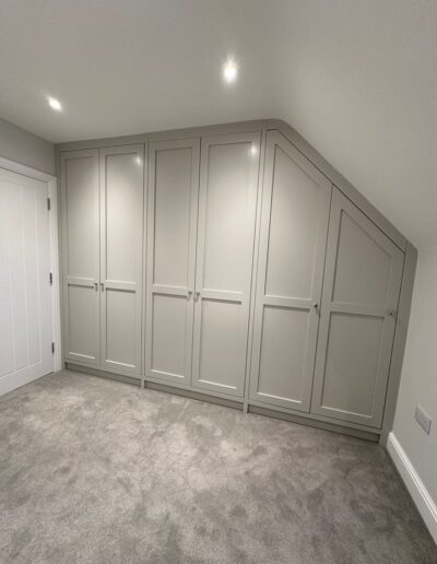 Angled Shaker-style bespoke fitted wardrobe finished in Morning Dew with oak internals & a combination of long & short hanging rails, shelf storage & shoe pull-out rack.