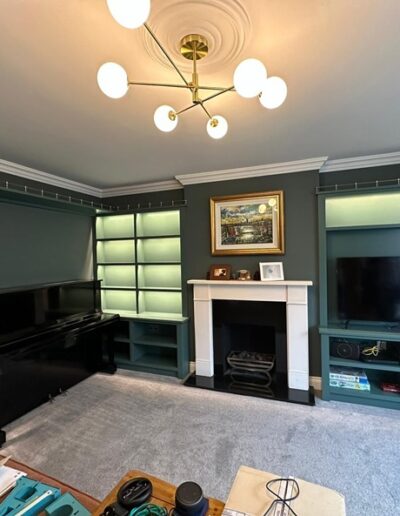 Bespoke fitted open shelving units with LED lights & space for a piano. Across the top of the units is a brass railing. Plus, an alcove unit with open shelving and space for TV and again LED lights and brass railing.