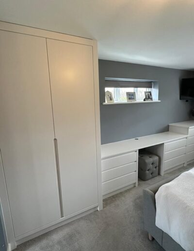 Full bedroom installation including custom-made wardrobes, dressing table with concealed laundry basket, chest of drawers and two bedside cabinets All pieces are in a modern handless style finished in Farrow and Ball Wevet