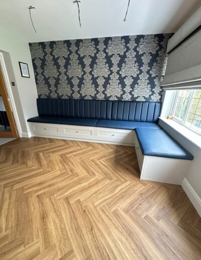 A bespoke banquette bench with a leather upholstered seat Grenada blue, featured Shaker-style drawers with LED lighting in the plinth finished in “Ammonite” by Farrow & Ball.
