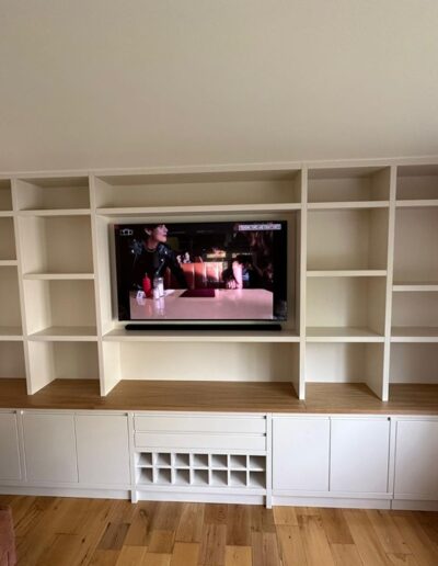 Custom-fitted media unit with handle-less cupboards and drawers, wine storage space, oak top, open shelving, and mounted TV, finished in Farrow & Ball's Dimity
