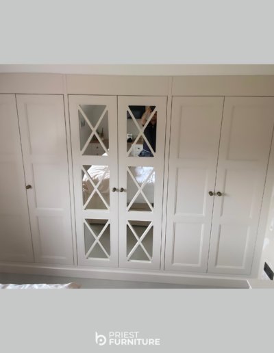 Bespoke fitted Shaker-style wardrobes with Fret Mirror doors painted in Slipper Satin by Farrow & Ball.